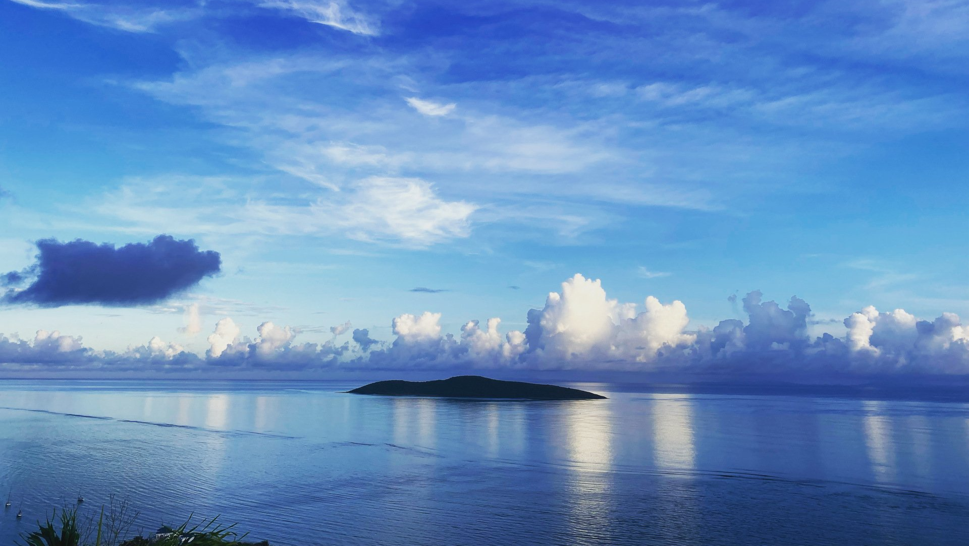 Calm blue water and an island beneath a bright cloud-filled sky